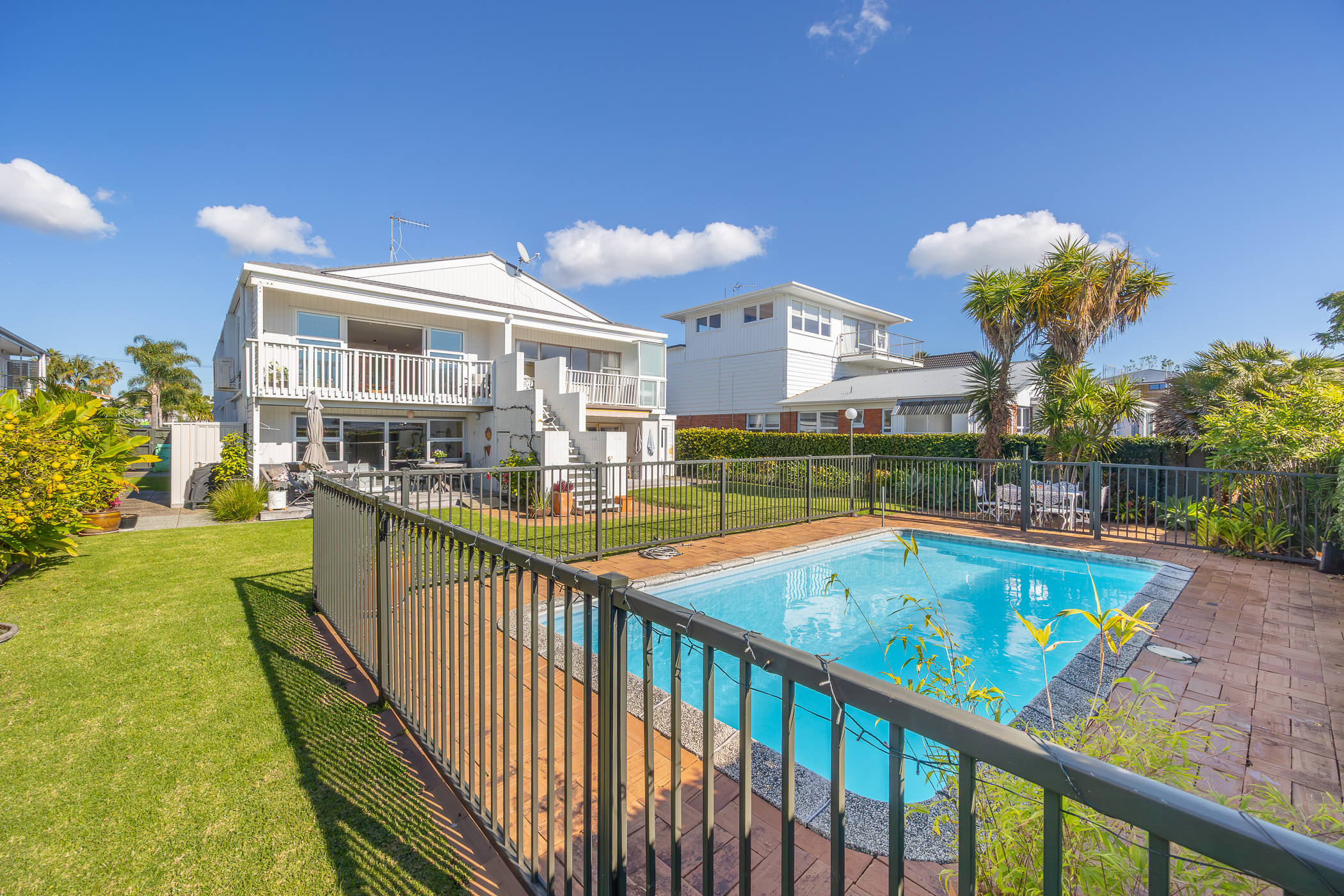 2 bedroom Unit at 4/22 Speight Road, Kohimarama. White multi-level unit with balconies, a fenced swimming pool, and green lawn.